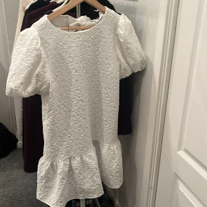 Vit klänning med blommigt mönster - Klänningen är helt slutsåld på deras hemsida och går ej att få tag på!!  söt vit klänning med puffiga kortärmar och ett blommigt mönster. Klänningen har en volangdetalj vid fållen som ger en lekfull touch. Perfekt för student eller bara somriga dagar! 