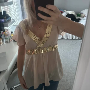 Beige topp med guldpaljetter - Säljer en elegant beige topp med glittrande guldpaljetter längs V-ringningen och midjan. Från hm med prislapp kvar aldrig använd 