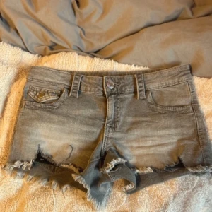 Grå jeansshorts från Gina Tricot - Säljer ett par snygga grå jeansshorts från Gina Tricot. De har en fransig kant och klassisk femficksdesign. Perfekta för en avslappnad stil.