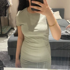 Ljus grön ribbad klänning - Snygg ljus grön ribbad klänning med korta ärmar och rynkade detaljer på sidorna. Perfekt för en stilren look. Klänningen har en tight passform som framhäver figuren.