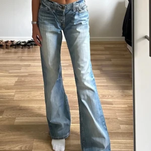 Blå jeans från Guess - Snygga blå jeans från Guess med en avslappnad passform. De har en elastisk midja då det är ett resårband man kan justera midjan själv, och bakfickor med knappdetaljer. 💙