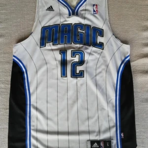 Vit Orlando Magic baskettröja från Adidas - Säljer en vit baskettröja från Adidas med Orlando Magic-tryck och nummer 12. Tröjan har blå och svarta detaljer samt ett randigt mönster. Perfekt för basketfans! 🏀storleken är S men skulle snarare säga M. 