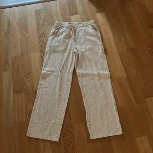 Beige linnebyxor från Grunt - Säljer ett par bekväma beige linnebyxor från Grunt. 10/10 skick aldrig använt helt som nya. Nypris 499kr säljer för 149kr Byxorna har en elastisk midja med snörning och en avslappnad passform. Perfekta för en avslappnad stil. Size M i ungdomsstorklek rekommenderad ålder 12/13 år. 