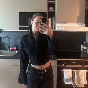 Svart omlottopp - Säljer en stilren svart omlottopp med långa ärmar. Toppen har en croppad passform och är perfekt för en trendig look. Den är enkel att matcha med olika outfits.