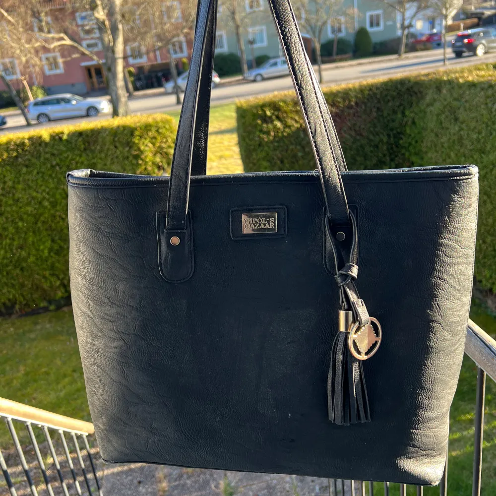 Snygg svart axelväska i skinn från Nicole Brown. Väskan har en stilren design med en dekorativ tofs och en praktisk dragkedja upptill. Perfekt för att bära dina dagliga nödvändigheter med stil.. Laukut & Käsilaukut.