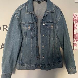 Blå oversized jeansjacka - Snygg blå jeansjacka med klassisk design och knappar framtill. Jackan har två bröstfickor med lock och knappar samt långa ärmar.