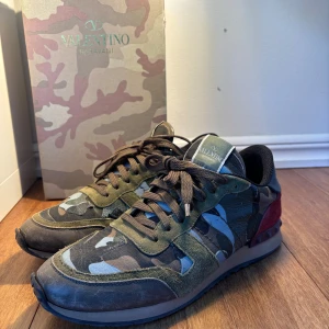 Valentino Rockrunner gröna - Snygga Valentino Rockrunner sneakers med ett coolt camouflagemönster i gröna och bruna toner. Skorna har en kombination av mocka och skinn, med röda detaljer på hälen. Perfekta för en stilren och trendig look.