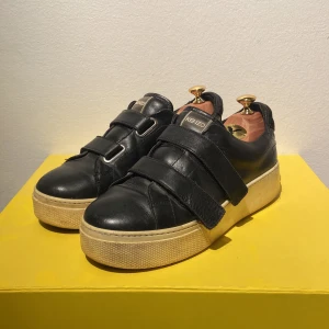 Svarta sneakers från Kenzo - Storlek 40, Snygga svarta sneakers från Kenzo med kardborreband och en robust vit sula. Skorna har en rund tå och är tillverkade i skinn, vilket ger en stilren och modern look. Perfekta för en avslappnad stil med en touch av lyx.
