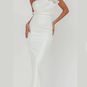 Vit axelbandslös långklänning - Elegant vit axelbandslös långklänning med draperad överdel och figurnära passform. Använd endast en gång som ombytte på min förlovning. Ren och hel.