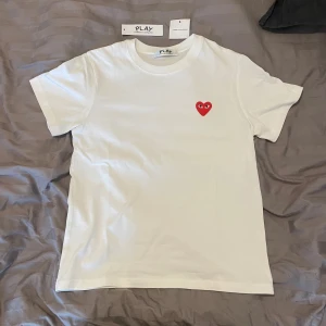 Vit t-shirt från Comme des Garçons Play - Vit t-shirt med klassisk passform från Comme des Garçons Play. Har det ikoniska röda hjärtat med ögon broderat på bröstet. Tröjan är i nytt skick och är köpt på vestiarie. Den är S men funkar även som xs