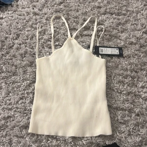 Vit ribbad linnetopp från Vero Moda - Säljer en vit ribbad linnetopp från Vero Moda med smala axelband och rak passform. Perfekt för sommardagar och enkel att matcha med olika outfits. Ny med tag kvar!