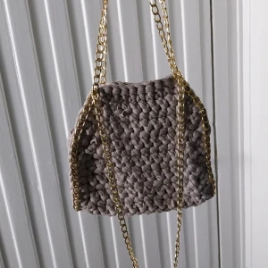 Beige virkad väska med guldkedja - Säljer en beige virkad handväska med grovt virkat material och en snygg guldfärgad kedja. Perfekt accessoar för att lyfta din outfit med en unik touch.