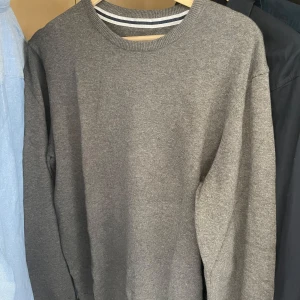 Grå stickad sweatshirt - En enkel och stilren grå sweatshirt med rund halsringning och långa ärmar. Perfekt för en avslappnad look och lätt att matcha med andra plagg. Mjuk och bekväm att bära.