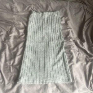 Ljusgrå ribbad långkjol - Säljer en ljusgrå långkjol med ribbat mönster. Kjolen har en rak passform och är mjuk och stretchig, perfekt för en avslappnad stil. Enkel att matcha med olika toppar och sneakers.