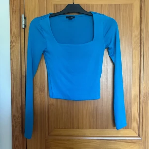 Blå långärmad croppad topp med fyrkantig ringning - Säljer en blå långärmad croppad topp med snygg fyrkantig ringning. Perfekt att styla med höga jeans eller kjol. Enkel och stilren design som passar till många tillfällen.