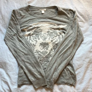 Grå stickad tröja med tigertryck från  forever21 - Säljer en grå stickad tröja från forever21 med ett stort tigeransikte i en vit nyans framtill. Tröjan har rund halsringning och långa ärmar. Perfekt för dig som vill ha en cool och unik look.det står att det är storlek m men jag skulle säga att det är storlek S. Skriv till mig för fler bilder eller övriga frågor! Pris kan diskuteras💕