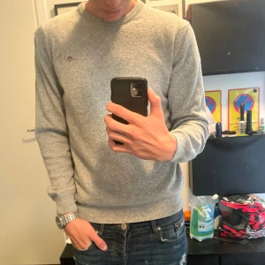 Grå stickad tröja från GANT - Säljer en stilren grå stickad tröja från Gant i storlek S med diskret logga på bröstet. Tröjan har rund halsringning och långa ärmar med ribbade muddar vid ärmslut och nederkant. Perfekt för lager-på-lager och enkel att matcha. Använd ett fåtal gånger, som ny skick. Nypris 1100kr🤩🤩🤩