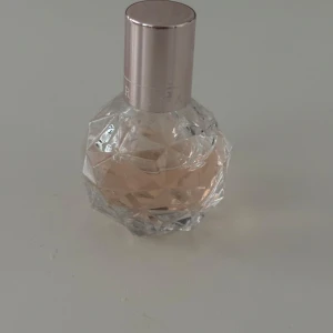Ariana Grande parfymflaska med diamantmönster - Säljer en parfym från Ariana Grande i en rund, diamantformad glasflaska med ljusrosa doftvätska. Flaskan har ett stilrent, ljusrosa metallock med artistens namn ingraverat. Perfekt för dig som gillar snygga och unika parfymflaskor.
