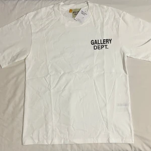 Vit t-shirt från Gallery Dept. - Vit t-shirt från Gallery Dept. med svart tryck på bröstet. Klassisk rund halsringning och korta ärmar. Enkel och stilren design som passar till det mesta.