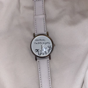 Vit klocka med humoristisk urtavla - Rolig klocka med vit läderrem och silverfärgat boett. Urtavlan har texten 'whatever, I'm late anyway.' och siffrorna ligger huller om buller. Perfekt accessoar för dig med humor.