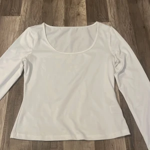 Vit långärmad topp med rundad urringning - En stilren vit långärmad topp med bred, rundad urringning. Tillverkad i ett mjukt och stretchigt material som sitter bekvämt mot kroppen. Perfekt att matcha med jeans eller kjol för en enkel och fräsch look.