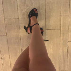 Svarta sandaler med klack och ankelrem - Säljer ett par svarta sandaler med hög klack och öppen tå. Skorna har en bred rem över tårna och en justerbar ankelrem med spänne. Materialet är mocka och sulan är platt framtill. Perfekta för dig som vill ha en stilren och bekväm klacksko.. går att klippa bort ankelremmen!❤️🥰