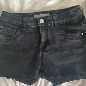 Svarta jeansshorts med fransig kant från Your Denim - Svarta jeansshorts med rå, fransig kant och klassisk femficksdesign. Shortsen har knapp och dragkedja framtill samt bälteshällor. Perfekta för varma dagar och enkel att matcha med olika toppar.