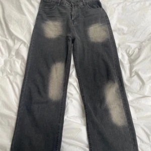 Gråa wide jeans med blekta detaljer - Säljer ett par gråa jeans med bred passform och tydliga blekta partier framtill och baktill. Jeansen har klassiska fickor och raka ben, samt extra fickor på benen. Perfekta för en avslappnad och trendig look.