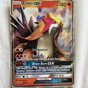 Pokémonkort Entei GX - Säljer ett samlarkort från Pokémon-serien, Entei GX med 180 HP. Kortet har en holografisk yta och visar Entei med attacker som Combustion, Fire Fang och Brave Burn GX. Perfekt för samlare eller Pokémon-fans.