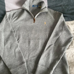 Grå stickad tröja med dragkedja från Polo Ralph Lauren - Säljer en helt oanvänd grå stickad tröja från Polo Ralph Lauren med halv dragkedja och broderad logga på bröstet. En lite mer sällsynt tröja, perfekt som ett lite finare plagg i garderoben. 