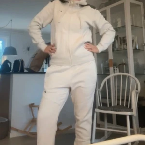 Vit hoodie och mjukisbyxor från Nike - Säljer en vit hoodie med dragkedja och matchande mjukisbyxor från Nike. Hoodien har långa ärmar, huva med snören och diskret Nike-logga på bröstet. Perfekt för en avslappnad stil. Byxorna är i storlek L och tröjan är i storlek S