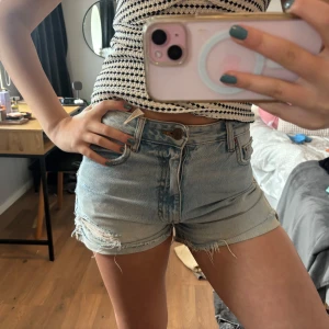 Ljusblå jeansshorts med slitningar - Säljer ett par ljusblå jeansshorts  och slitningar framtill.  knapp och dragkedja finns. Perfekta för varma dagar och enkel att matcha med olika toppar. Dem är i bra skick! Hör av er vid frågor