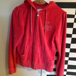 Rosa velourhoodie från Lipsy London - Säljer en rosa hoodie i mjuk velour från Lipsy London. Jackan har dragkedja, huva, två fickor fram och dekoreras med strassdetaljer och hjärtmotiv både fram och bak. Perfekt för en trendig och bekväm look.