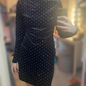 Svart sammetsklänning med strassdetaljer - Svart sammetsklänning med långa ärmar och glittrande strass över hela klänningen. Djup urringning i ryggen och figurnära passform. Aldrig använd.