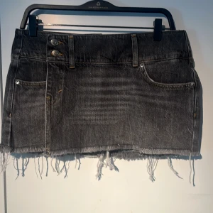 Grå jeanskjol från Weekday - Säljer en grå jeanskjol från Weekday med råa kanter och dubbla knappar framtill. Kjolen har klassiska fickor både fram och bak samt en kort passform.