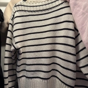 Randig stickad tröja från Gina Tricot - Säljer en vit stickad tröja med svarta ränder från Gina Tricot. Tröjan har en klassisk rund halsringning och långa ärmar. Perfekt för en avslappnad och stilren look.