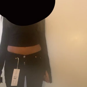 Svarta jeansbyxor med låg midja - Säljer ett par svarta jeansbyxor med låg midja och klassisk femficksdesign. Byxorna är bootcut och stängs med knapp och dragkedja. Perfekta för en stilren och enkel look.