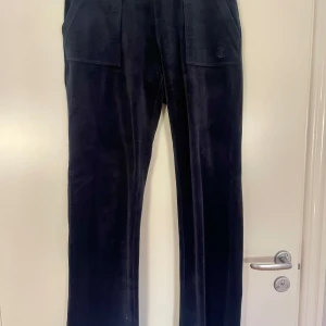 Mörkblå Juicy Couture byxor - Säljer ett par mörkblå byxor från Juicy med raka ben och fickor både fram och bak. Byxorna har en klassisk look och är tillverkade i ett mjukt material som påminner om manchester. Perfekta för dig som gillar stilrena och bekväma plagg. Ens ringen runt snöret är borta och finns ett litet brännmärke på knät
