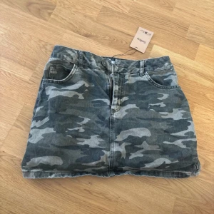 Camo denimkjol från Subdued - Säljer en camouflagemönstrad jeanskjol från Subdued i gröna och grå toner. Kjolen har klassisk femficksdesign, bälteshällor och knapp med Subdued-logga. Perfekt för dig som gillar streetstyle och vill sticka ut lite extra. midwaist och midjemått är 38 cm!