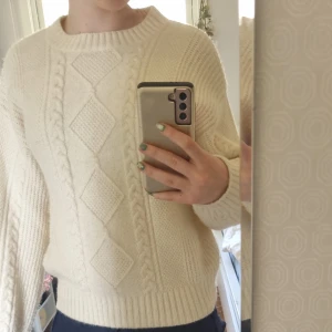Vit stickad tröja från H&M - Säljer en krämvit stickad tröja från H&M med klassiskt kabelstickat mönster och diamantdetaljer framtill. Tröjan har rund halsringning, långa ärmar och breda ribbade muddar vid ärmslut och nederkant. Perfekt för kyliga dagar!Har användit några gånger men i nyskick.  Frakt ingår inte. Säljer för att jag har växt ur dem. 