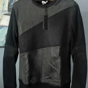 Helt ny Helmut Lang tröja, Nypris 3700kr - Säljer en svart sweatshirt från Helmut Lang i storlek M. Tröjan har unika texturerade paneler och meshdetaljer framtill, samt rund halsringning och långa ärmar. Butikspriset är 3700kr. Notera däremot att materialet i översta panelen ser ut som att det har släppts lite då den bara stått. 