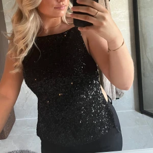 Svart glittrig paljettopp - Säljer en svart glittrig topp med paljetter och smala axelband. Toppen har en rak halsringning och är ärmlös, perfekt för att sticka ut på festen. Snygg och trendig modell som passar till många olika outfits.