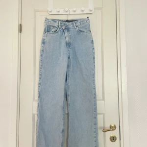 Ljusblåa wide jeans - Säljer ett par ljusblåa jeans med hög midja och raka, vida ben. Klassisk femficksmodell med gylf och knapp framtill. Perfekta för en avslappnad och trendig look.
