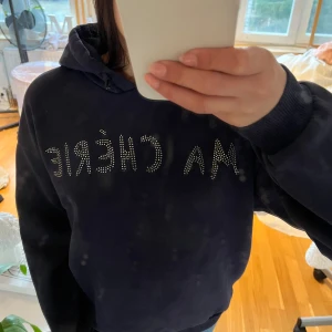 Svart hoodie med strassdetaljer - Svart hoodie med huva och texten 'MA CHÉRIE' i strass på bröstet. Mjuk och bekväm modell med långa ärmar och ribbade muddar. Perfekt för en avslappnad stil. Använd mindre än 10ggr. Säljer pga inte kommit till användning.