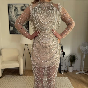 Glittrig långklänning med pärlor och paljetter - Säljer en fantastisk långklänning i nude med transparenta partier, täckt av glittrande paljetter och pärlor i flera lager. Klänningen har lång ärm och figurnära passform. Storlek xs-34 har haft den en gång bara.