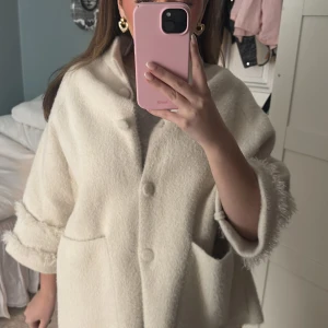 Vit oversized ulljacka med knappar från Jackie - Säljer en krämvit oversized jacka i ullmix med stora knappar framtill och två rejäla fickor. Jackan har uppvikta ärmar och en rak, boxig passform som ger en cool och avslappnad look.