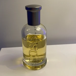 Hugo Boss Bottled Eau de Toilette - Klassisk herrparfym från Hugo Boss med fräsch och maskulin doft. Flaskan är genomskinlig med silverfärgad kork och tydlig BOSS-logga på framsidan. Innehållet är ljusgult och flaskan har rundad form.