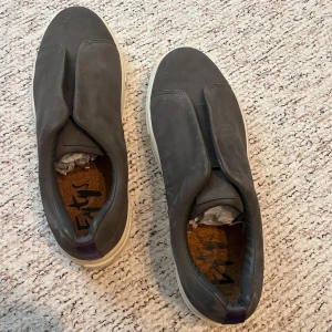 Grå slip-on sneakers med vit sula - Snygga grå slip-on sneakers från eytys med vit platt sula och diskret lila detalj på hälen. Helt oanvända, säljer billigt har för mycket skor 