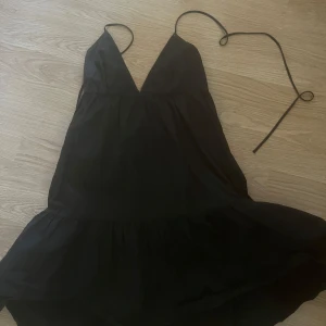 Svart kort klänning från Zara - Säljer en svart kort klänning från Zara med smala axelband och v-ringad hals. Klänningen har en luftig passform och volang nertill, perfekt för varma dagar.