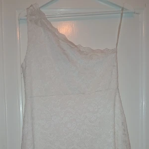 Vit spetsklänning från Model Behaviour - Säljer en vit spetsklänning från Model Behaviour i storlek M. Klänningen har oneshoulder-design och är täckt av vacker spets. Materialet består av 90% nylon och 10% elastan med foder i 100% polyester. Perfekt för somriga tillfällen! Endast prövad till student år 2022 men bara hängt sen dess. Möts bara upp i närheten av Stockholm södra. 